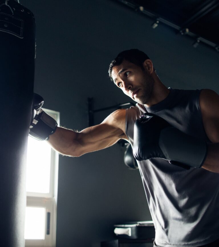 Man training on a heavy bag with boxing gloves at Gold’s Gym Cheyenne focused on powerful strikes in a dark training space