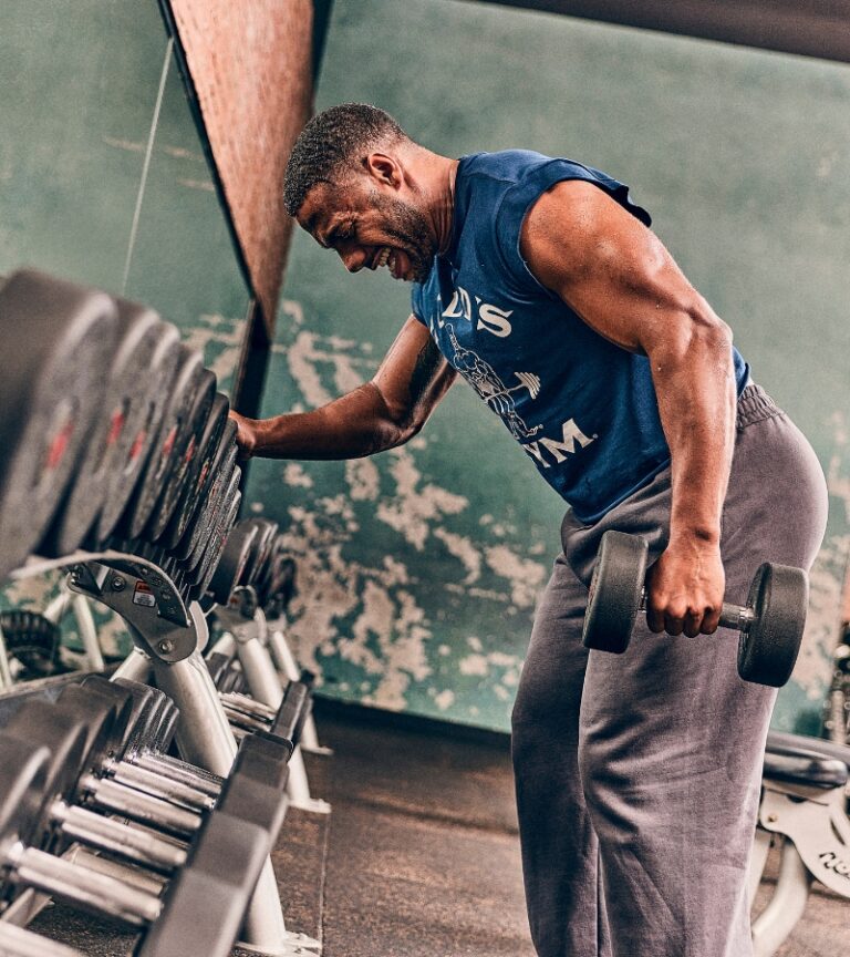 Man performing a heavy dumbbell row in the free weight area at Gold’s Gym Cheyenne with rows of dumbbells in front of him